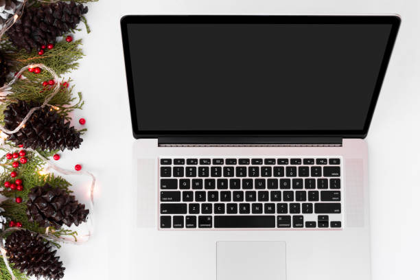 istock Computer laptop mobile display on table with isolated white screen for mockup in Christmas time. Christmas tree, gifts, decorations in background. 873856774