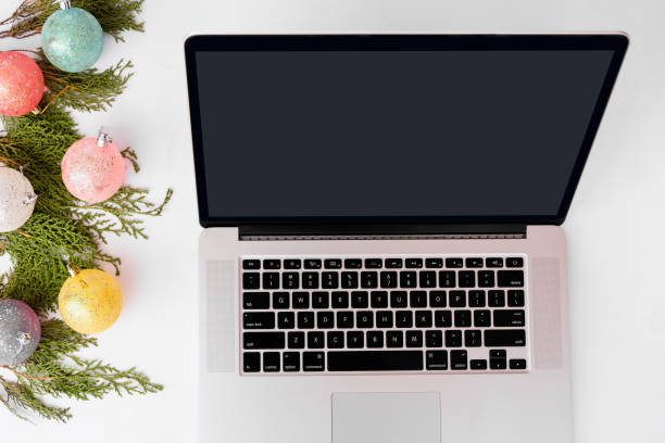 istock Computer laptop mobile display on table with isolated white screen for mockup in Christmas time. Christmas tree, gifts, decorations in background. 873857582