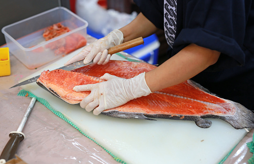 Chef slicing raw fish for salmon sushi on a cutting board.
