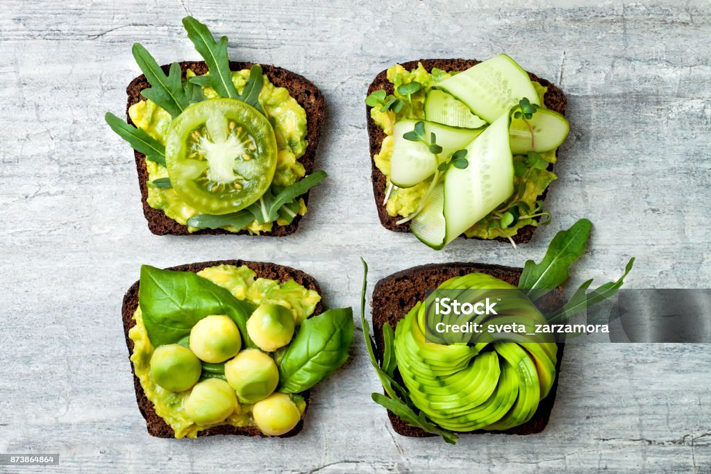 Fresh avocado toasts with different toppings. Healthy vegetarian breakfast with rye wholegrain sandwiches Avocado Stock Photo