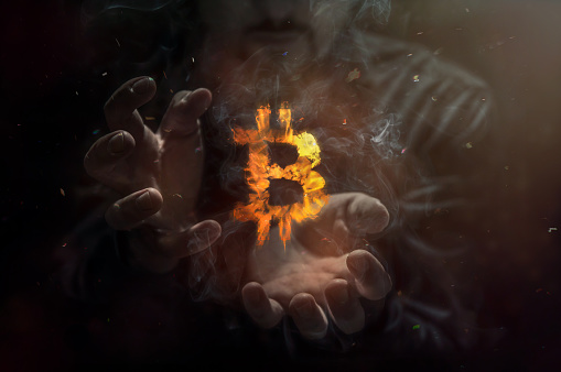 Burning symbol of bitcoin with man in the background. Conception of risk management in money trading at currency market