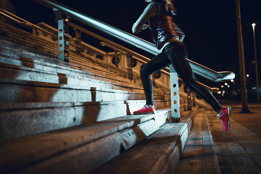 Sportswoman running up on concrete stairs. Night time