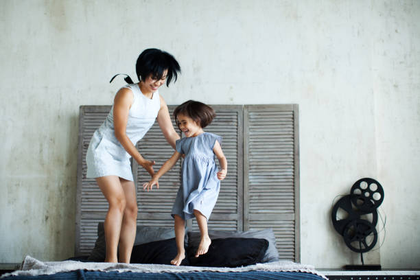 parenting relaxado - mother and daughter holding hands on bed - fotografias e filmes do acervo