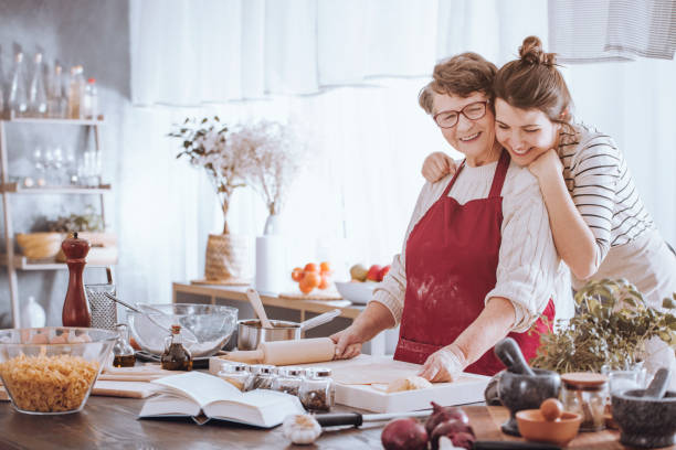 nipote che abbraccia la nonna in cucina - grandmother senior adult family domestic kitchen foto e immagini stock