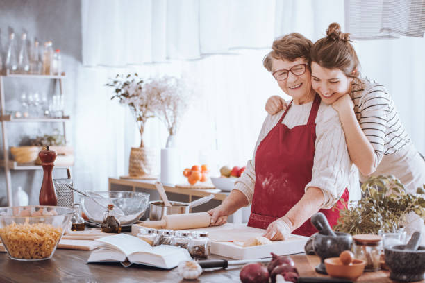 Granddaughter hugging grandmother in the kitchen Granddaughter hugging grandmother while making cake together in the kitchen recipe photos stock pictures, royalty-free photos & images