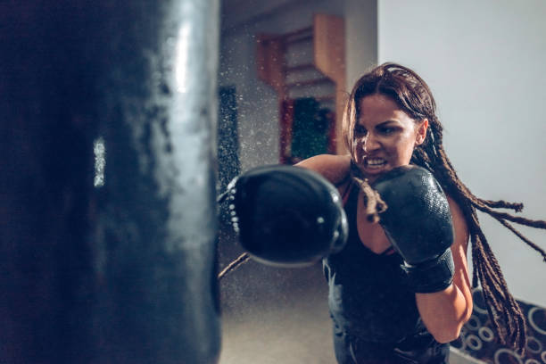 female kickboxer training with a punching bag - toughness imagens e fotografias de stock