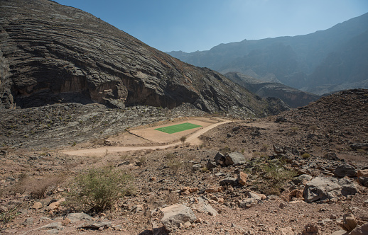 Green football field in the middle of desert mountains. Nizwa, Oman.