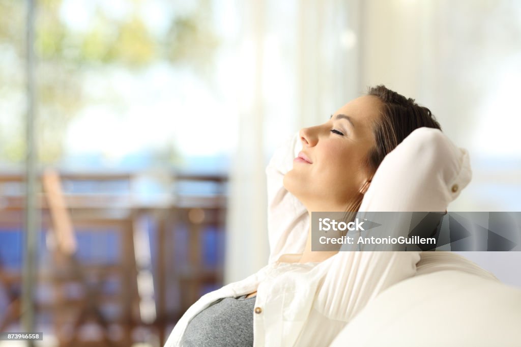 Woman relaxing on vacations in an apartment Side view portrait of a happy woman relaxing sitting on a couch on vacations in an apartment on the beach Women Stock Photo