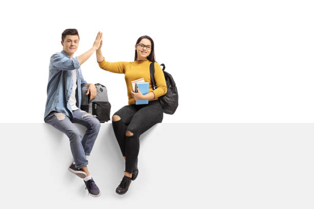 Teenage students seated on a panel high-fiving each other and looking at the camera isolated on white background