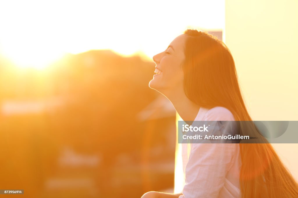 Woman breathing at sunset in a balcony Side view portrait of a happy woman breathing deep fresh air at sunset in a house balcony Sunlight Stock Photo