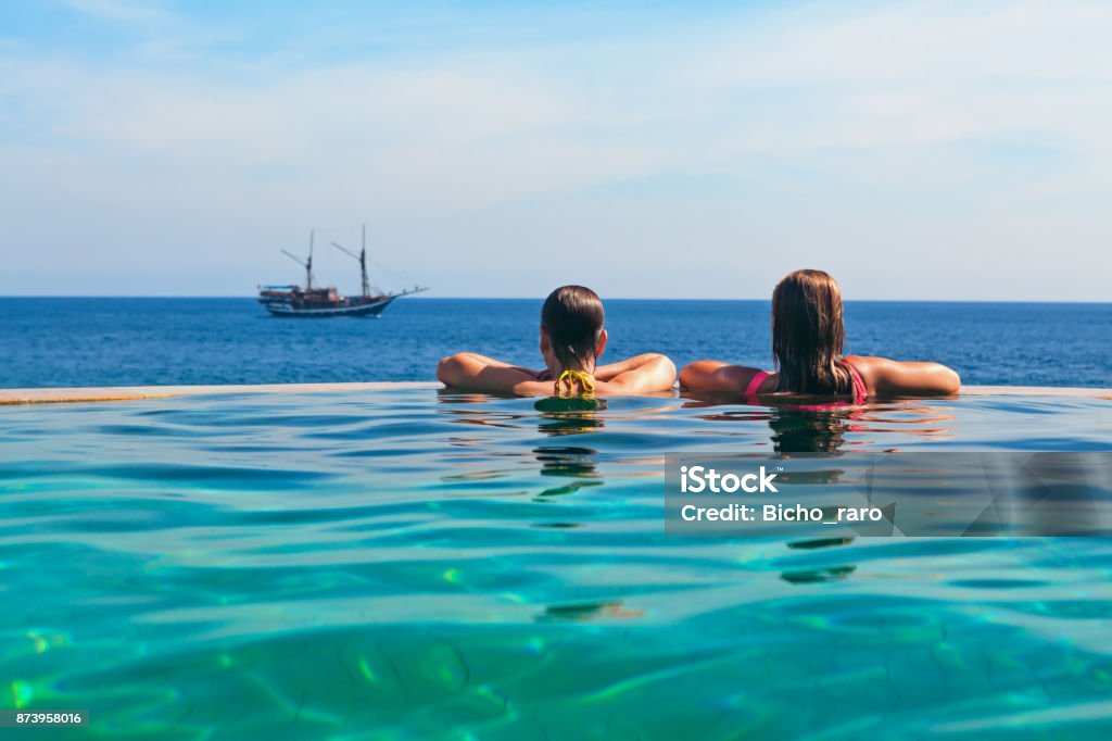 Relaxing in infinity swimming pool with sea view Happy young woman on summer beach holiday relaxing in luxury spa resort in infinity swimming pool with sea view. Healthy lifestyle, family travel background. Sailing yacht tropical island cruise. Cruise - Vacation Stock Photo