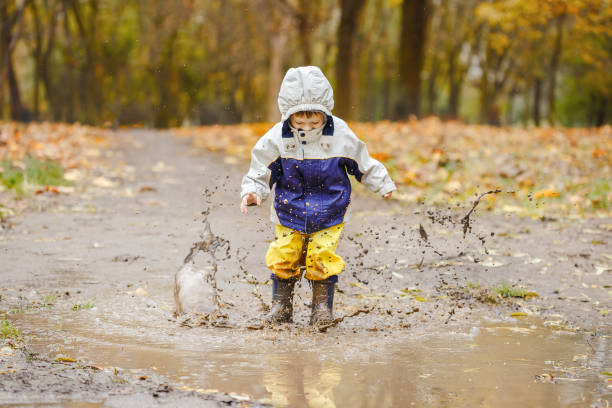 botas de niña feliz saltando sobre los charcos de goma - puddle fotografías e imágenes de stock