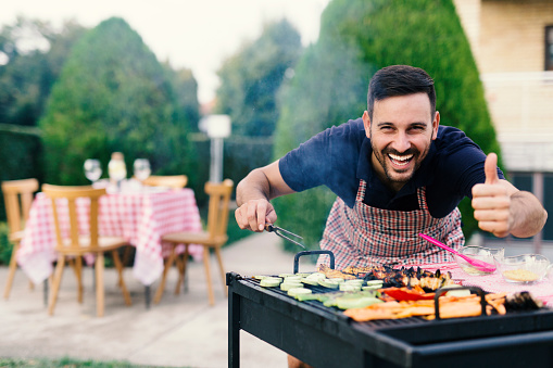 Young man making barbecue at his backyard, thumb up