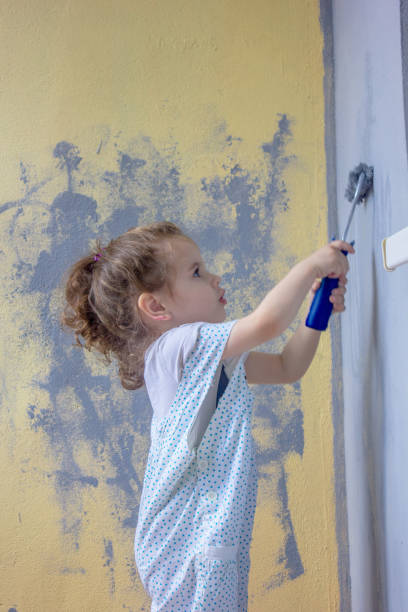 istock Little kid girl paints wall by paint roller 874016582