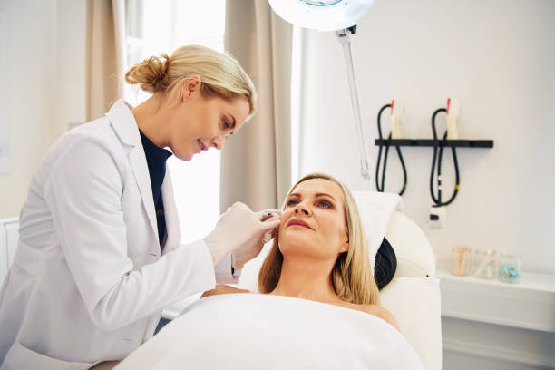 Doctor doing botox injections on a mature client's face Young female doctor doing botox injections on the face of a mature woman lying on a table in a beauty clinic beauty clinic stock pictures, royalty-free photos & images