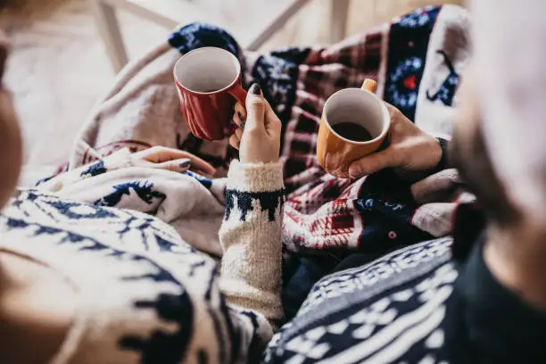 Photo of Close up of couple holding mugs with coffee, wearing Santa's hat