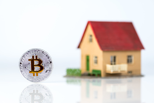 Kiev, Ukraine - October 23, 2017: Bitcoin and private house model at light background. Real estate theme. Concept of Buying a property for crypto currency.