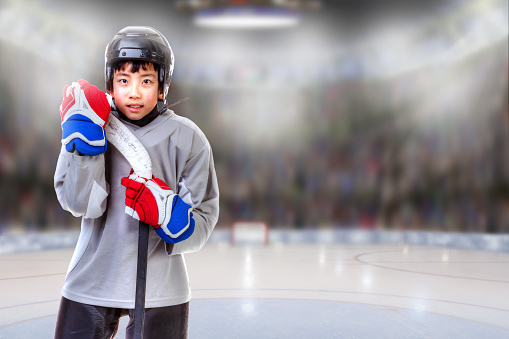 Junior hockey player posing on ice in sports arena. Shallow depth of field on background and copy space.