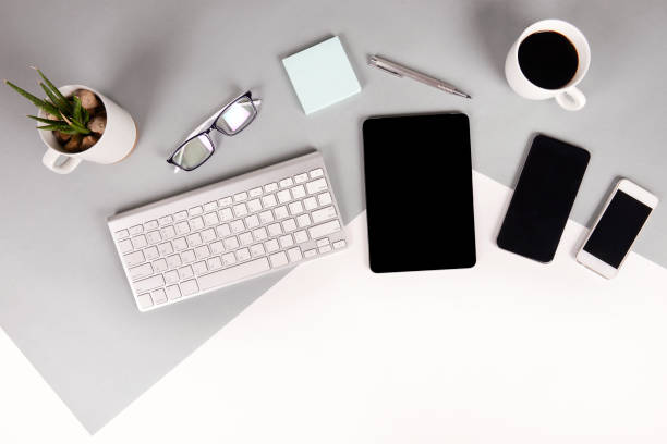 istock Flat lay photo of Office table with keyboard, notebook, digital tablet, mobile phone, Pencil, eyeglasses  on modern two tone (white and grey) background. Desktop office mockup concept. 874047468
