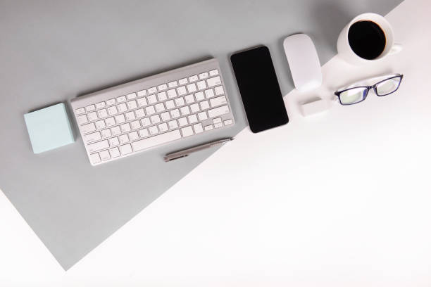 istock Flat lay photo of Office table with keyboard, notebook, digital tablet, mobile phone, Pencil, eyeglasses  on modern two tone (white and grey) background. Desktop office mockup concept. 874047680
