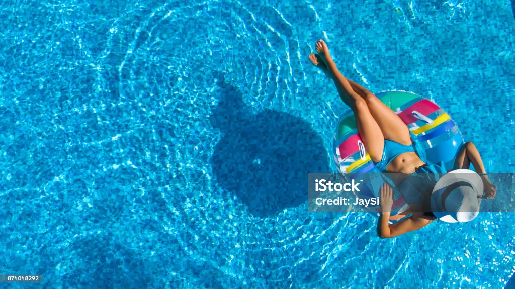 Aerial top view of beautiful girl in swimming pool from above, relax swim on inflatable ring donut and has fun in water on family vacation Family Stock Photo