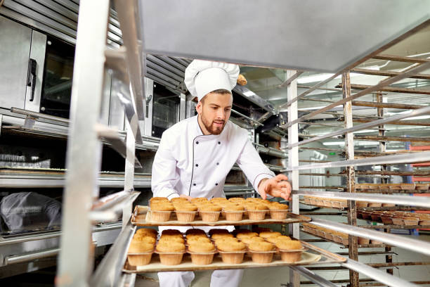 istock Baker man with a tray of cupcakes in his hands at work in Christ 874051674