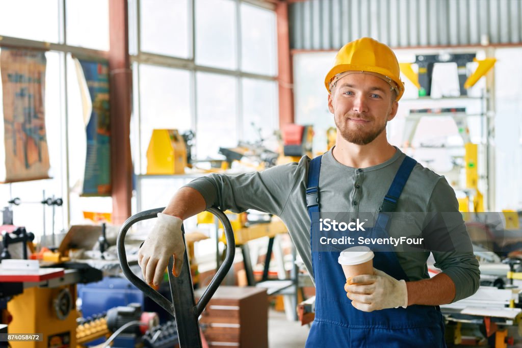 Smiling Young Workman on Break Portrait of young worker taking break in factory workshop looking at camera holding coffee cup and smiling happily Manufacturing Occupation Stock Photo