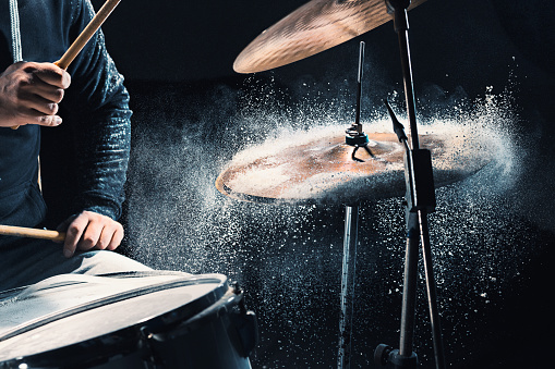 The hands of drummer rehearsing on drums before rock concert. Man recording music on drum set in studio with show effect in the form of flour
