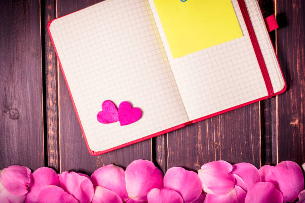 istock blank note book close-up with rose leaves, hearts and copy space on wooden background. Spring summer border template. mockup floral background. sale, greeting and celebration card concept. 874063582