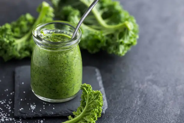 delocious  kale pesto sauce and fresh raw leaves on dark background, selective focus