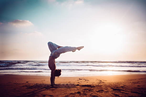 спортивный мужчина, практикующий йогу на пляже на закате - 20s athlete muscular build balance стоковые фото и изображения