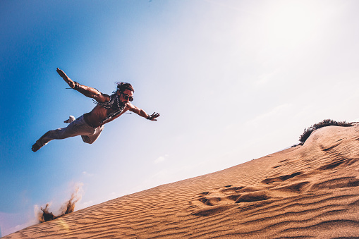 Young man with futuristic retro goggles practising parkour and doing jumps over desert sand dunes