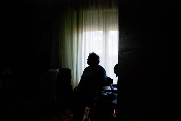 senior mujer sola en el cuarto oscuro - soledad fotografías e imágenes de stock