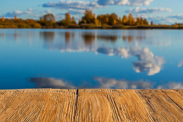 istock Empty rustic wood table top on  blurred colorful autumn landscape background with fall forest and blue sky with cloudscape reflection on the lake. Can montage or display your products 874103482