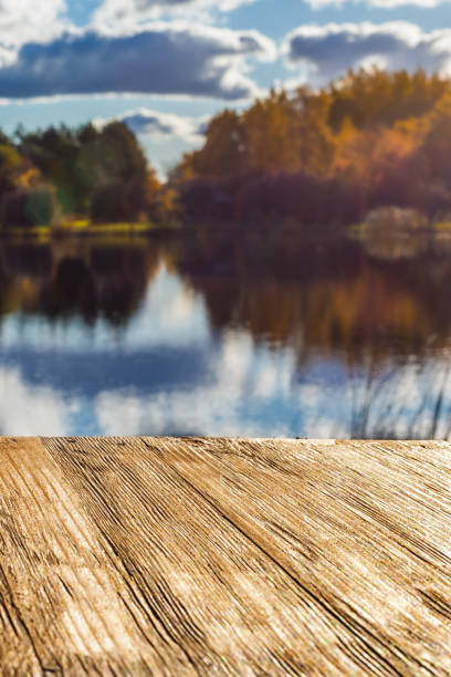 istock Empty rustic wood table top on  blurred colorful autumn landscape background with fall forest and blue sky with cloudscape reflection on the lake. Can montage or display your products 874103594