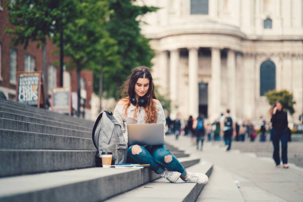 Schoolgirl in UK studying outside Young girl sitting at the steps and using lap top campus stock pictures, royalty-free photos & images