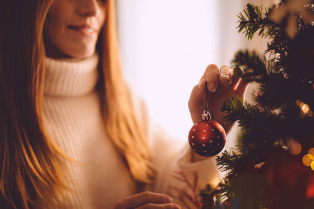 Smiling ginger woman decorating Christmas tree with red Christmas ball
