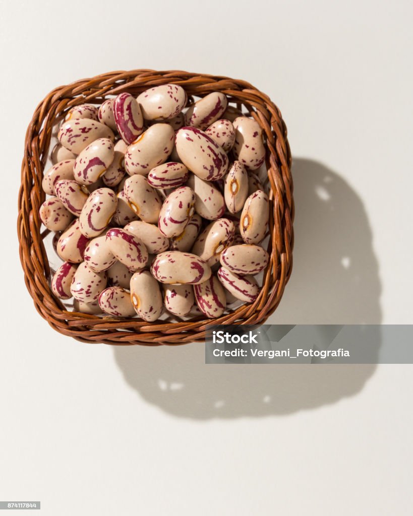 Phaseolus vulgaris is scientific name of Sugar Bean legume. Also known as Feijao Rajado or Frijol Canaval. Wicker basket with grains. Top view, hard light. Above Stock Photo