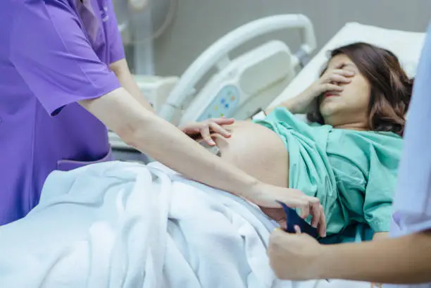 Doctor examining belly of expectant mother in hospital room. Thailand.