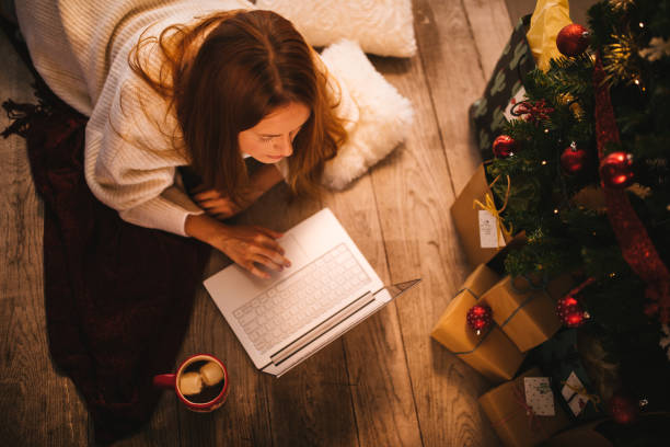 женщина покупке рождественских подарков онлайн с помощью ноутбука под елкой - lying down women laptop freedom стоковые фото и изображения