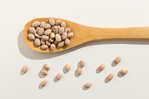 Phaseolus vulgaris is scientific name of Pinto Bean legume. Also known as Frijol Pinto and Feijao Carioca. Healthy grains on a wooden spoon. White background.