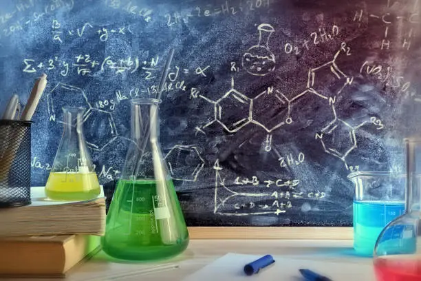 Classroom desk and drawn blackboard of chemistry teaching with books and instruments. Chemical sciences education concept. Horizontal composition. Front view