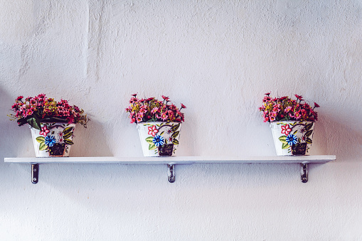 Retro styled white metal flowerpots with small pink flowers on the wooden shelf.