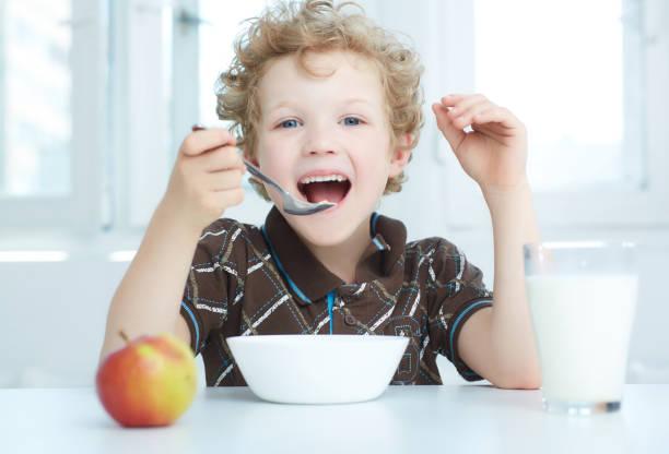 niño comiendo cereales desayunando en la cocina. - beauty beautiful braids dairy product fotografías e imágenes de stock