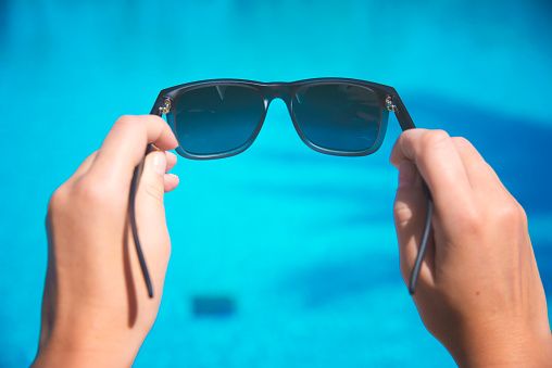 Woman holds sunglasses on pool background