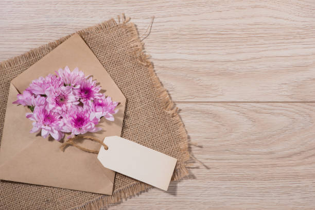 istock Blank white paper tag with brown envelope and pink flowers on wooden table. 874231102