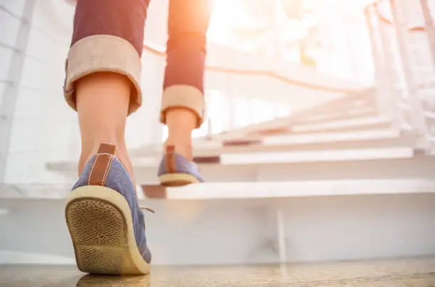 Photo of Young adult woman walking up the stairs with sun sport background.