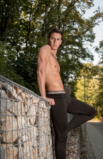 One young handsome man posing, shirtless forest fitness body muscular rocks, looking sideways