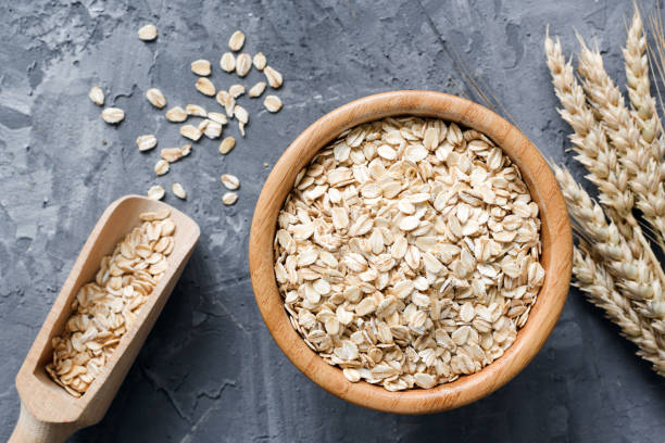 Rolled oats or oat flakes in wooden bowl on stone background. Rolled oats or oat flakes in wooden bowl and golden wheat ears on stone background. Top view, horizontal. Healthy lifestyle, healthy eating, vegan food concept nut food photos stock pictures, royalty-free photos & images