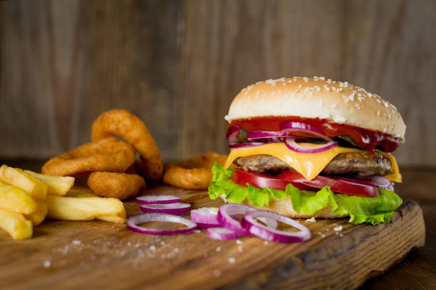 cheeseburger, french fries and onion rings on wooden chopping board over wooden backdrop - beer hamburger american culture beef imagens e fotografias de stock